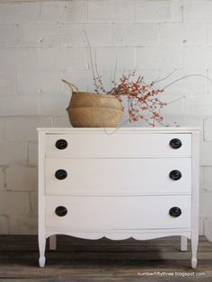 a white dresser with black knobs and a basket sitting on it's top