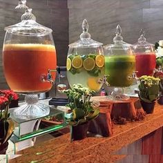 several different types of drinks on display in glass jars and vases with flowers around them