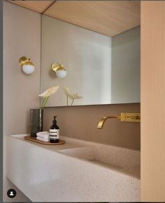 a bathroom sink sitting under a mirror next to a vase with flowers on top of it