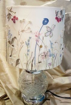 a glass lamp with flowers painted on it sitting on a cloth covered tableclothed surface