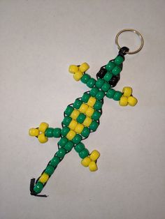 a green and yellow beaded lizard ornament on a white surface with a black keychain