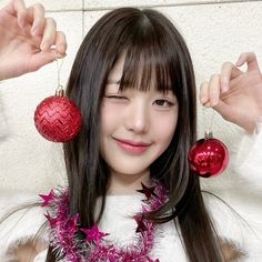 a girl with long black hair holding two red ornaments