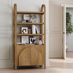 a wooden book shelf with books and pictures on it next to a door in a white room