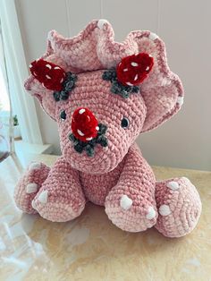 a pink crocheted elephant with red flowers on its head sitting on a table