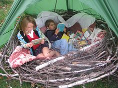 two children are reading books in a teepeed tent with branches on the ground