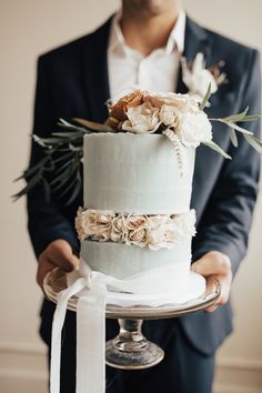 a man in a suit holding a wedding cake with flowers on the top and bottom