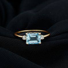 an aqua blue topazte and diamond ring sits on a black cloth