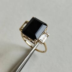 ITEM DESCRIPTION: >> The Ring is made from Solid 14K Yellow Gold. Gemstone used is absolutely natural and ethically sourced. >> Natural White Topaz and Black Onyx in prong setting is studded on it with utmost precision. >> This is a minimalist design which makes it a hassle free and everyday jewelry. >>Center Gem: Black Onyx Center Gem size: 12x10 mm Center Gem weight: 4.95 ct >>Side gemstone: White Topaz Side Gems size: 6x3 mm Gem weight: 1.05 carats Gold purity: 14K (58.33% approx.) Gold weigh Black Emerald-cut 14k Gold Jewelry, Formal Black Sapphire Ring In 14k Gold, Black Sapphire Ring In 14k Gold, 14k Gold Black Gemstone Rings, 14k Gold Black Ring With Center Stone, Black 14k Gold Ring With Center Stone, Black Onyx Jewelry, White Topaz Rings, Onyx Jewelry