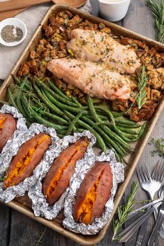 a pan filled with meat and green beans on top of tin foil next to utensils