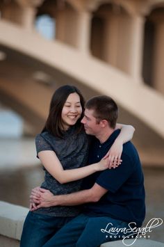 a man and woman sitting next to each other in front of a bridge