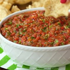 a person dipping salsa into a white bowl with tortilla chips on the side