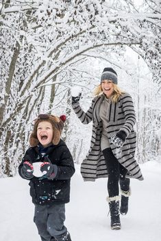 a woman and child walking through the snow in winter clothes, holding onto mitts