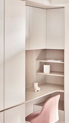 a pink chair sits in front of a white desk and cabinets with shelving on the wall