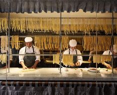 three chefs are preparing pasta in a kitchen