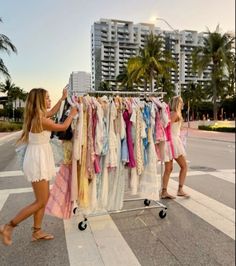 two women are trying to sell clothes on a rack in the middle of the street