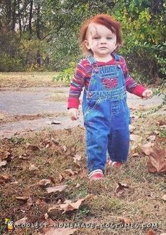 a young child with red hair and blue overalls standing in leaves on the ground