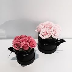 two black boxes with pink roses in them sitting on a table next to each other