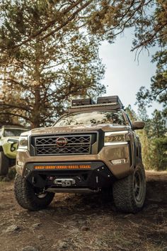 two trucks parked in the woods next to each other on dirt and grass covered ground