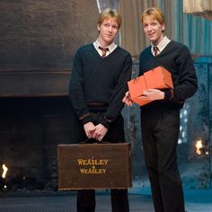 two young men standing next to each other in front of a fire place holding boxes