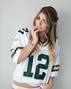 a beautiful young woman in a green and white football uniform posing for the camera with her hand on her cheek