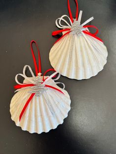 two seashell ornaments with red ribbon on them