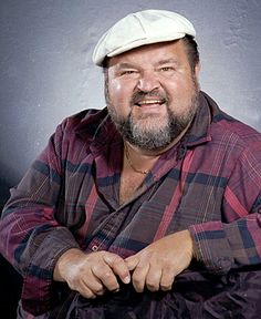 a man with a beard and a plaid shirt is posing for a photo in front of a gray background