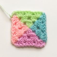 a crocheted square is hanging from a string on a white surface with the colors of pink, blue, green and yellow