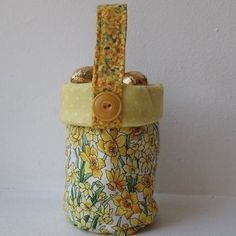 a yellow and white flowered basket with buttons on the top is sitting against a wall