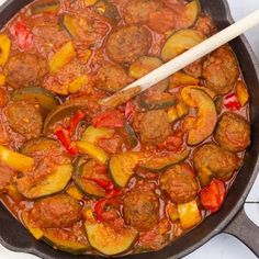 a pan filled with meatballs and vegetables next to a wooden spoon