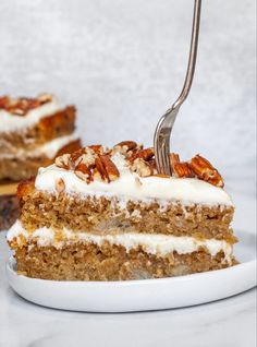 a piece of carrot cake with white frosting and pecans on the top slice