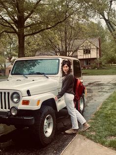 a woman standing next to a white jeep parked on the side of a road in front of a house