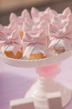 cupcakes with pink bows are on a cake plate in front of other cupcakes