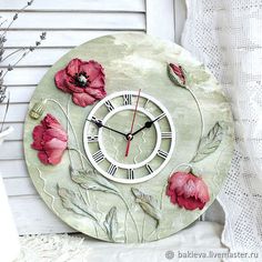 a clock with flowers painted on it sitting next to a white curtain and windowsill