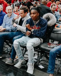 two men sitting in the stands at a basketball game, one with dreadlocks on his head