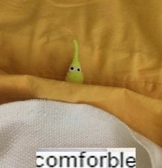 a green stuffed animal sitting on top of a yellow blanket next to a white pillow