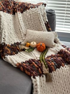 a knitted blanket sitting on top of a couch next to a pillow and pumpkins