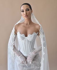 a woman wearing a white wedding gown and veil with gloves on her hands, standing in front of a beige background