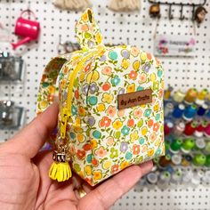 a person holding up a small bag in front of a wall full of sewing supplies