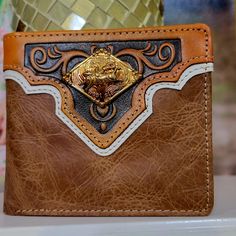 Western Genuine Leather bullrider logo Wallet  Bifold   Hand tooled design floral and geometric. Comes in a box. Brand new western wallet *             Bi-fold style *             plain   pattern on the back *             Made of genuine hand tooled leather *             Measures 41/2 inches long by 3 1/2 inches wide, about 3/8 inch thick (closed) *            5  credit card slots,                2 cash compartments .             2 ID clear slots .              1 zippered coin pocket .               1 large zippered pocket .               1 extra pocket at the back. .              Beautiful Longhorn concho .            Comes in a Western style box. Tooled Leather Roper Wallet, Vintage Hand Tooled Leather Trifold Wallet, Western Style Leather Rectangular Wallet, Western Style Brown Trifold Wallet With Card Slots, Cool Belt Buckles, Western Leather Wallet With Card Slots, Luxury Hand Tooled Brown Wallets, Fun Wallets, Rodeo Cowboy