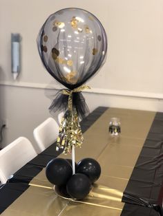 black and gold balloons are on top of a table with white chairs in the background