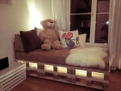 a teddy bear sitting on top of a couch in front of a window with white curtains