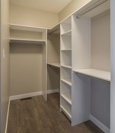 an empty walk in closet with white shelving and wood flooring on the side