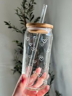 a hand holding a clear cup with hearts on the side and a straw in it