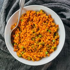 a bowl filled with rice and peas on top of a gray cloth next to a spoon