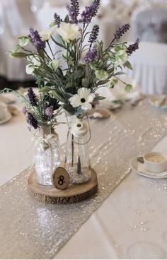 there is a vase with flowers in it on top of a wooden stand at the table