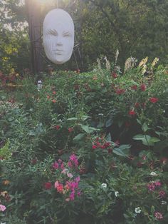 a garden with flowers, plants and a large white head in the middle of it