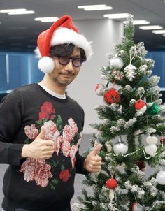 a man wearing a santa hat standing next to a christmas tree