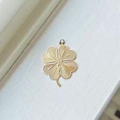 a gold four leaf clover charm sitting on top of a window sill in front of a white wall