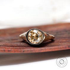 a gold ring with an old - fashioned diamond sits on a piece of wood in front of a white background