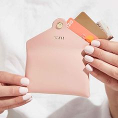 a woman holding a pink purse with credit cards in it's pocket and two hands